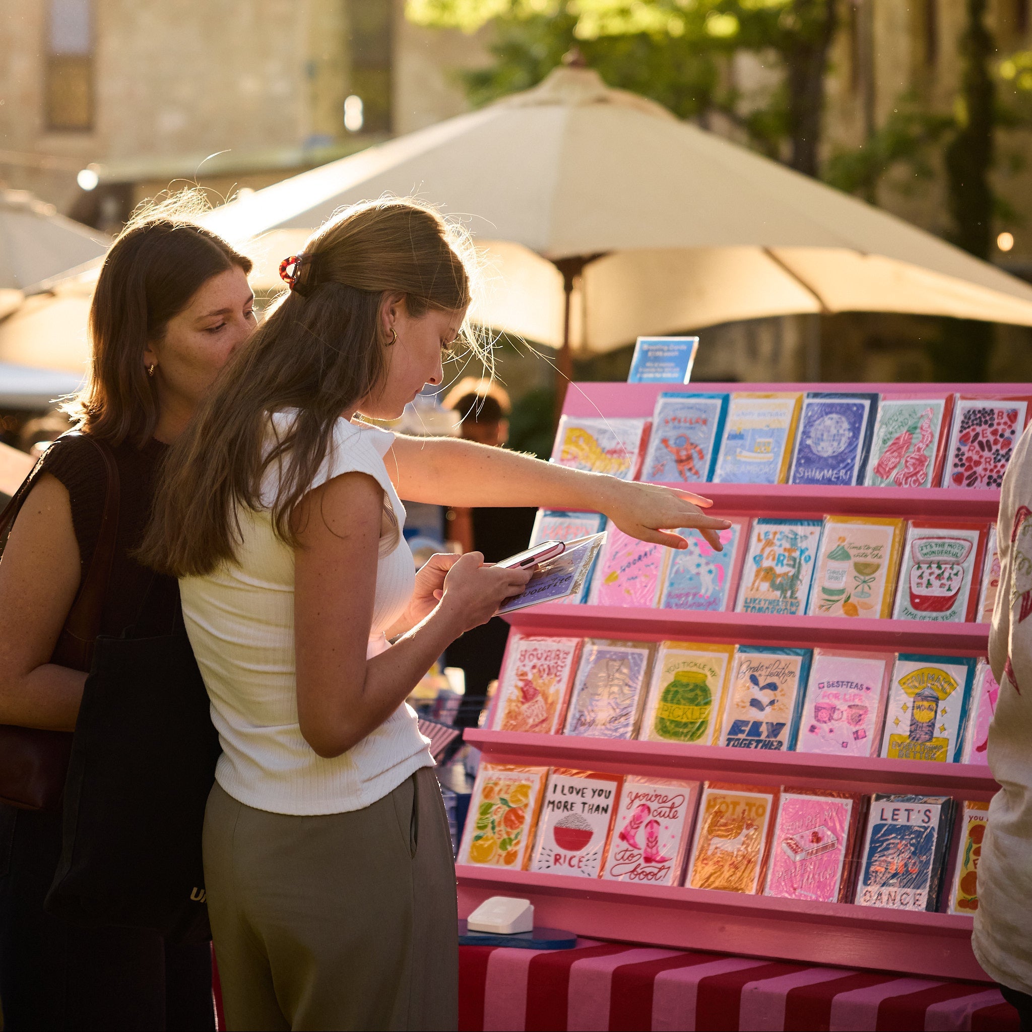 Two women looking at greeting cards in an outdoor market setting.